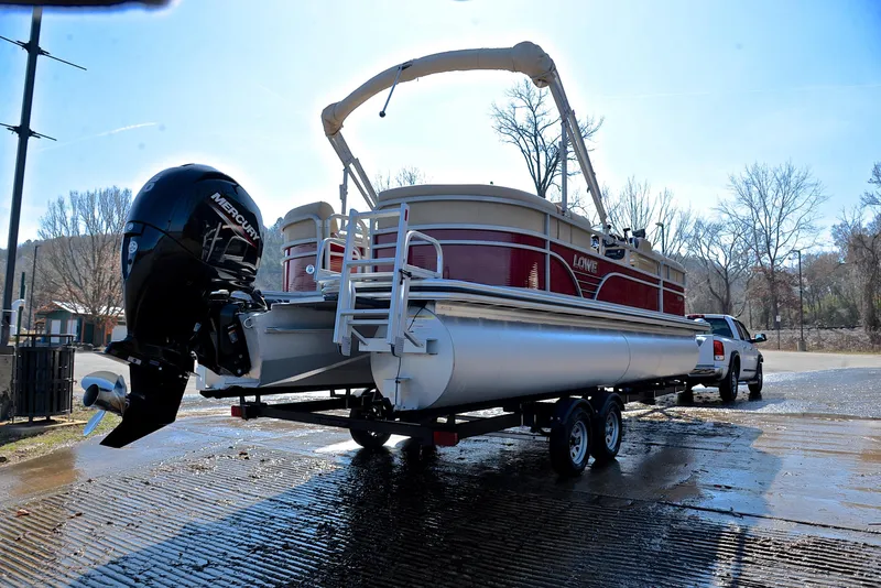Slide: The Image of 2021 Lowe SS250 pontoon boat on trailer, parked near a lake, with a powerful outboard motor. - 14