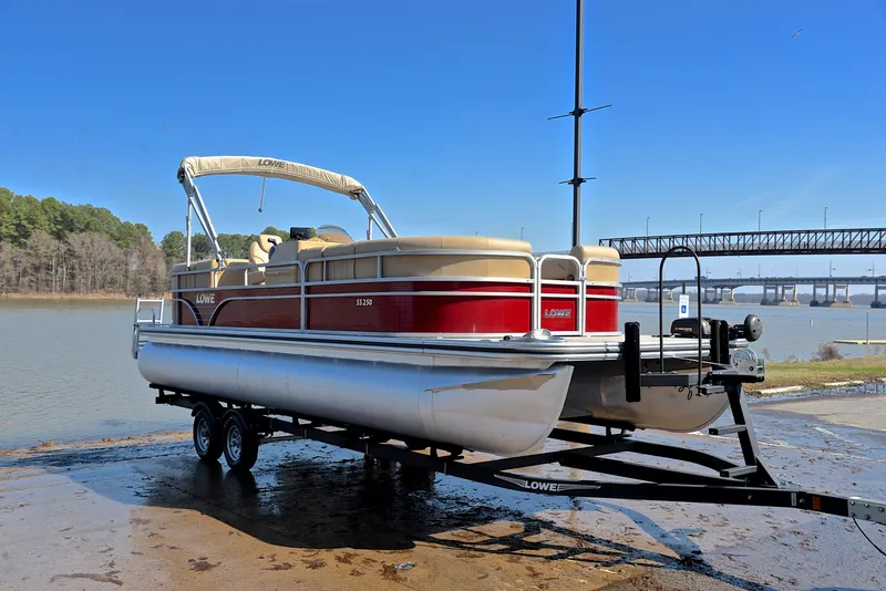 Slide: The Image of 2021 Lowe SS250 pontoon boat on trailer by a lake with a bridge in the background. - 16