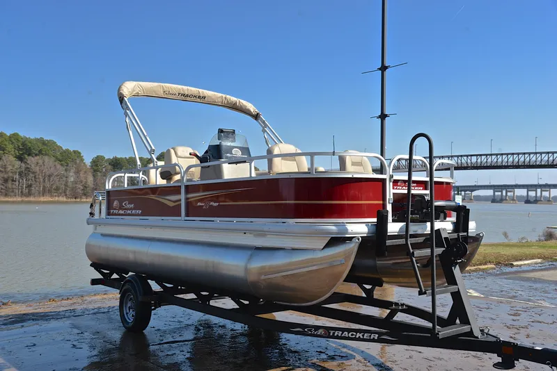Slide: The Image of 2024 Sun Tracker BASS BUGGY 18 pontoon boat on trailer by a lake. - 16