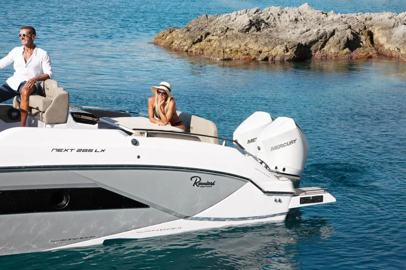 Slide: The Image of 2025 Ranieri NEXT 285 XL boat cruising in clear blue waters near rocky shore. - 14
