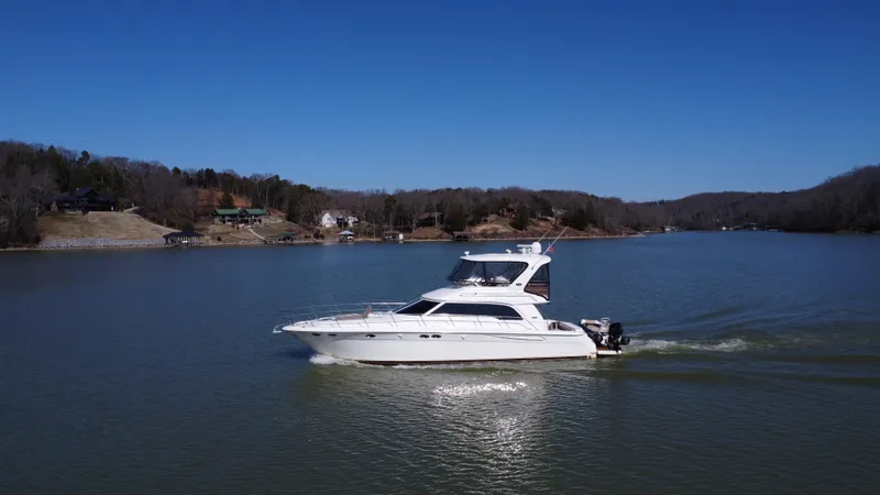 Slide: The Image of 2001 Sea Ray 480 Sedan Bridge cruising on a serene lake under a clear blue sky. - 3