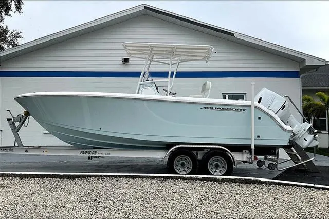 Slide: The Image of 2025 Aquasport 2200 Center Console boat on trailer, parked outside a building. - 34