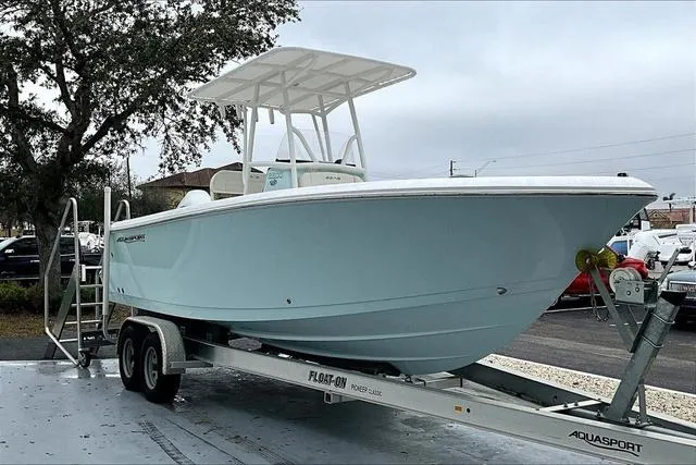Slide: The Image of 2025 Aquasport 2200 Center Console boat on trailer, light blue hull, parked outdoors. - 4