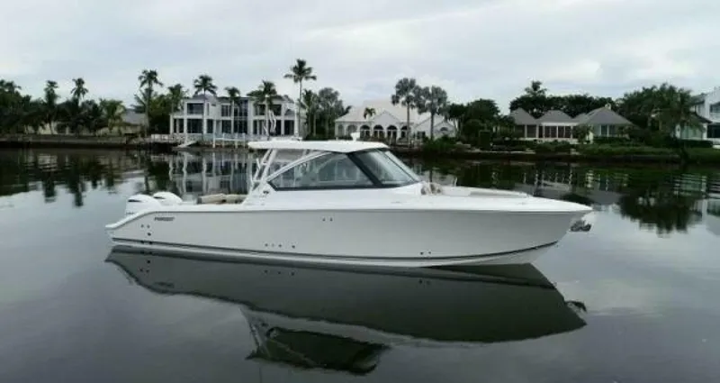 Slide: The Image of 2019 Pursuit DC 325 Dual Console boat on calm water, with waterfront homes in the background. - 0
