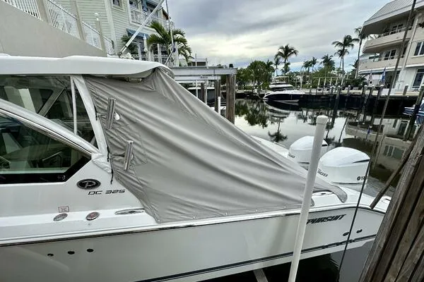 Slide: The Image of 2019 Pursuit DC 325 Dual Console boat docked with cover, surrounded by waterfront homes. - 31