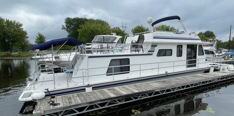 Slide: The Image of 2003 Gibson 50 Classic houseboat docked on a calm lake under cloudy skies. - 5