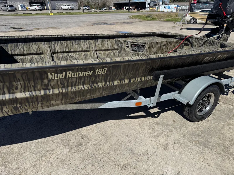 Slide: The Image of 2025 SeaArk Mud Runner 180 boat on trailer, camo design, parked outdoors. - 14