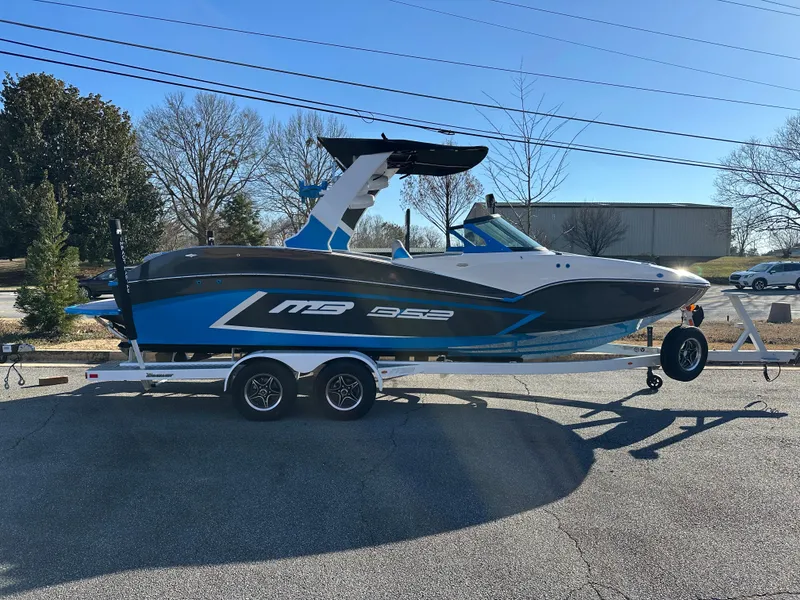 Slide: The Image of 2022 MB B52 23 Alpha boat on trailer, blue and white design, parked outdoors. - 2