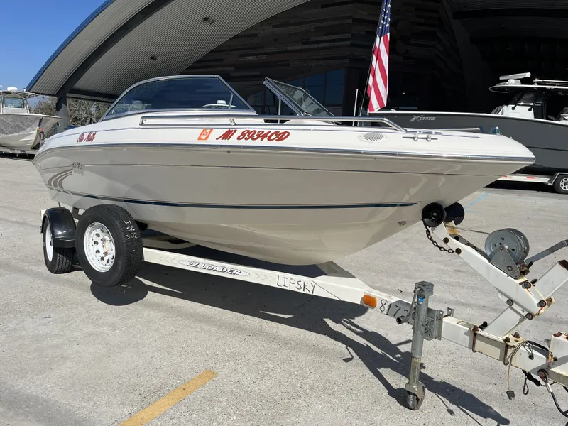 Slide: The Image of 1997 Sea Ray 185 boat on trailer, parked outdoors with American flag in background. - 9