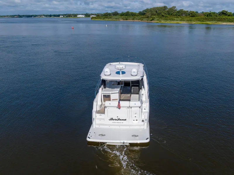 Slide: The Image of 2021 Regal 38 Grande Coupe yacht cruising on a serene lake with lush shoreline. - 15