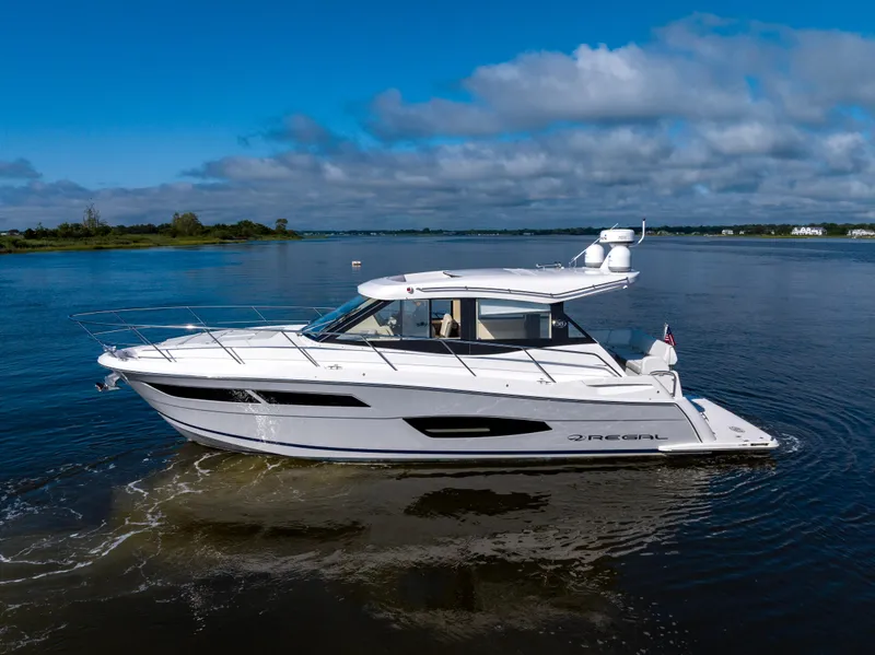 Slide: The Image of 2021 Regal 38 Grande Coupe yacht cruising on a serene lake under a blue sky. - 18