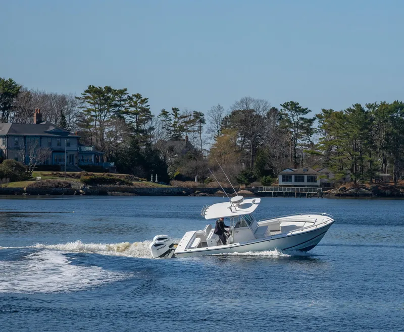 Slide: The Image of 2003 Regulator 26 Forward Seating boat cruising on a scenic lake with houses and trees. - 23