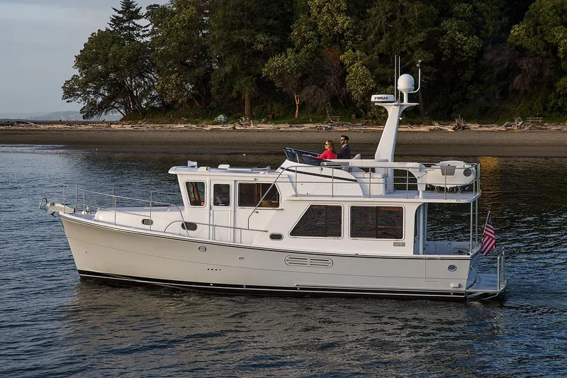 Slide: The Image of 2026 Helmsman Trawlers 38E Pilothouse cruising near a forested shoreline. - 0