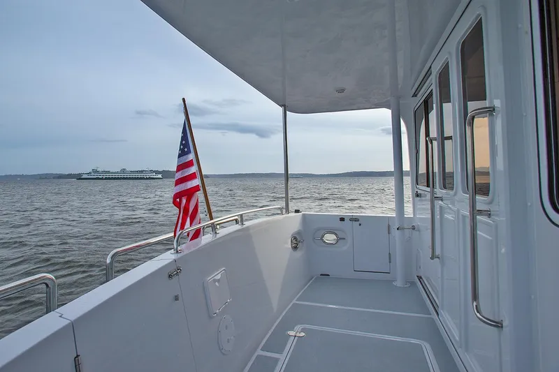 Slide: The Image of 2026 Helmsman Trawlers 38E Pilothouse deck with American flag, overlooking calm waters. - 17