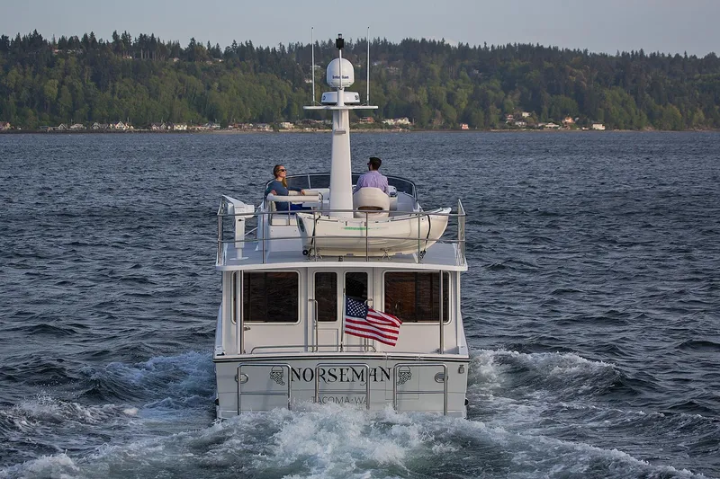Slide: The Image of 2026 Helmsman Trawlers 38E Pilothouse cruising on a scenic lake with forested shoreline. - 7
