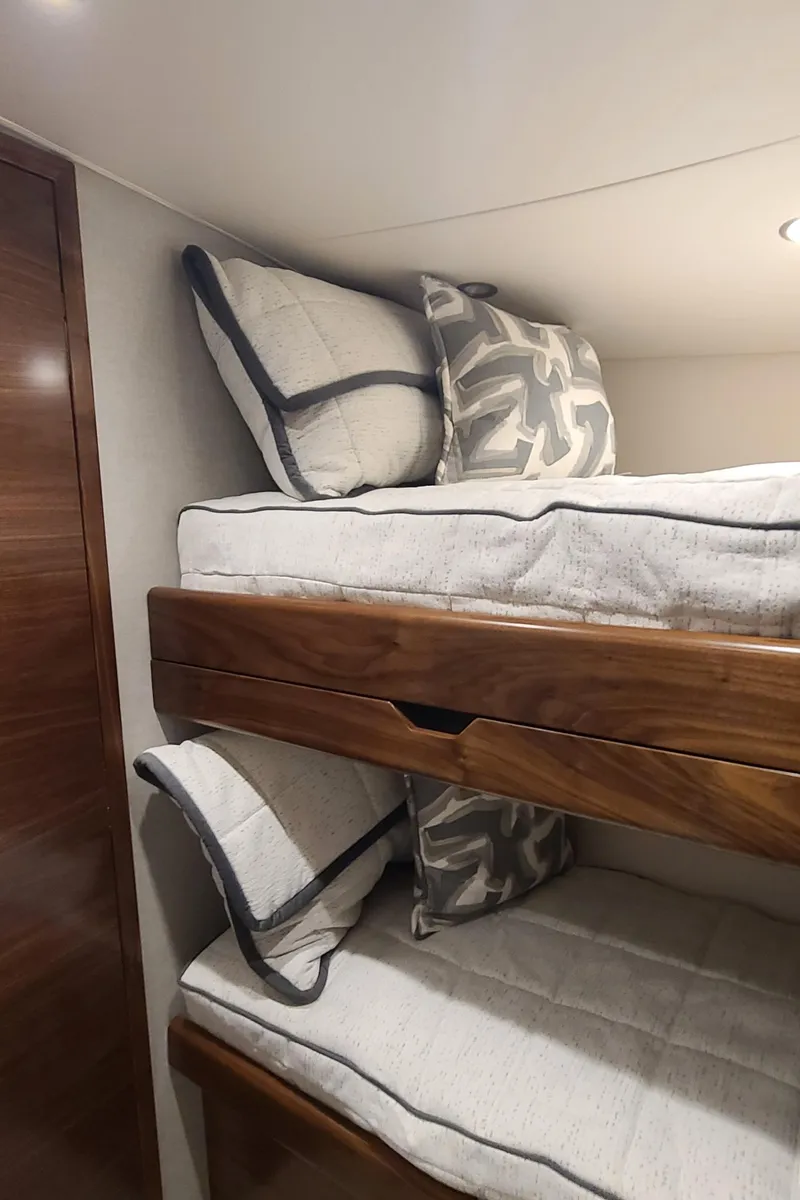 Slide: The Image of 2024 Viking 54 Convertible yacht interior with wooden bunk beds and plush pillows. - 7