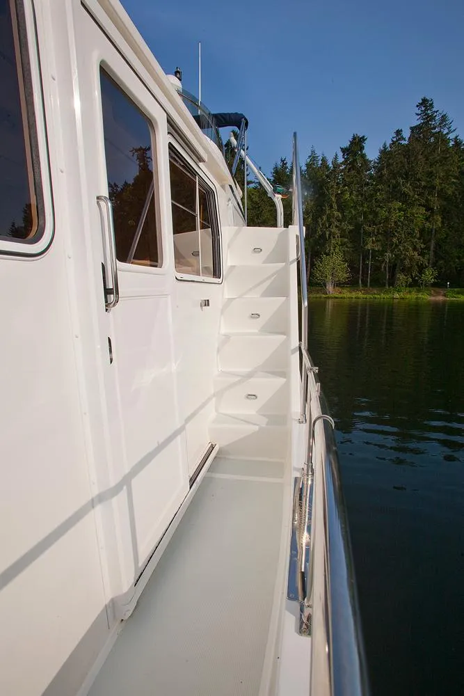 Slide: The Image of 2026 Helmsman Trawlers 43E Pilothouse yacht exterior with stairs and scenic water view. - 14