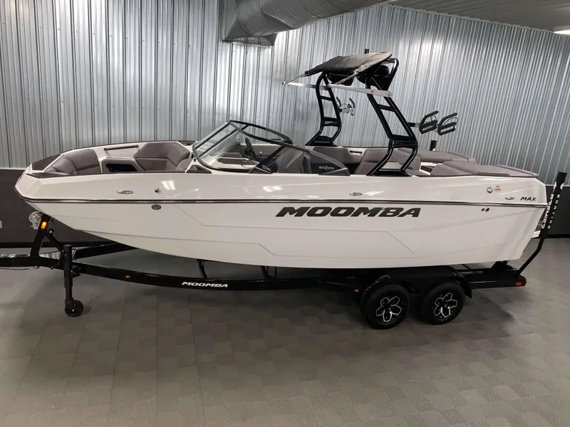 The Image of 2025 Moomba Max boat in showroom, sleek design, white exterior, black trailer. - 1