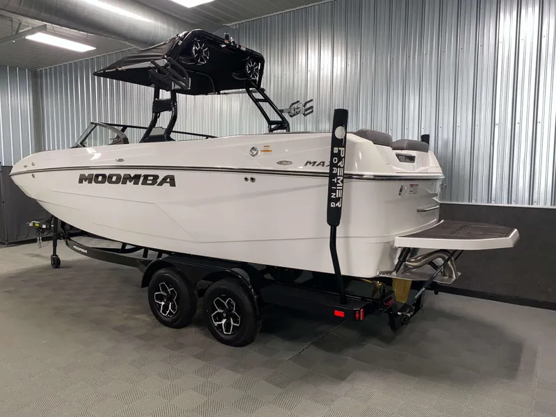 Slide: The Image of 2025 Moomba Max boat in showroom, white exterior, dual-axle trailer, sleek design. - 22