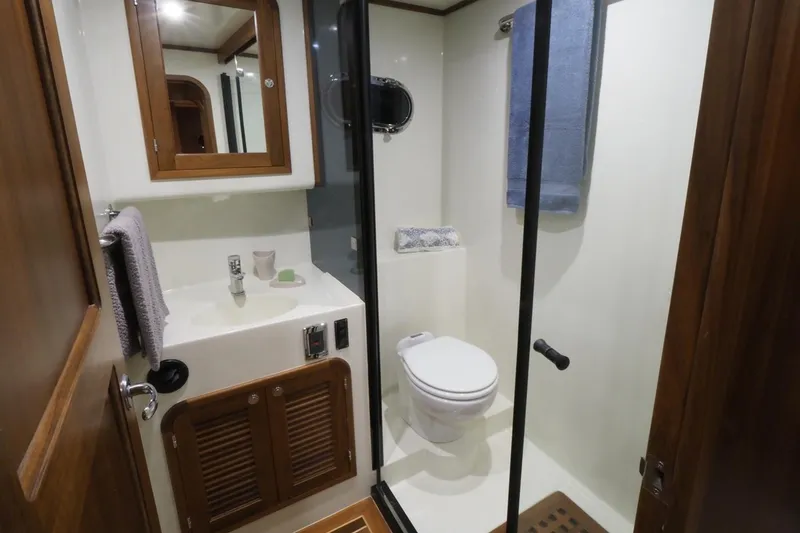 Slide: The Image of 2026 Helmsman Trawlers 46 Pilothouse bathroom with shower, toilet, and wooden cabinetry. - 47