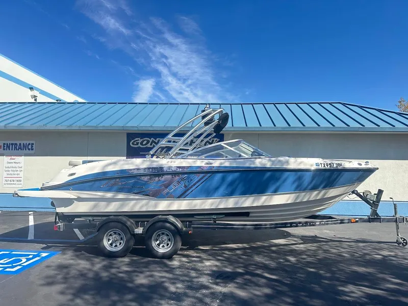 Slide: The Image of 2012 Bayliner 235 Bowrider boat on trailer, blue and white design, parked outdoors. - 0