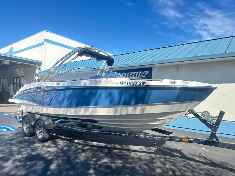 Slide: The Image of 2012 Bayliner 235 Bowrider on trailer, parked outdoors under clear blue sky. - 1