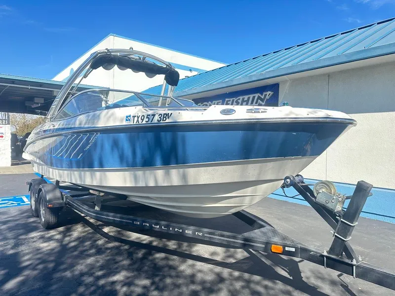 Slide: The Image of 2012 Bayliner 235 Bowrider on trailer, blue and white, parked outdoors under clear sky. - 4