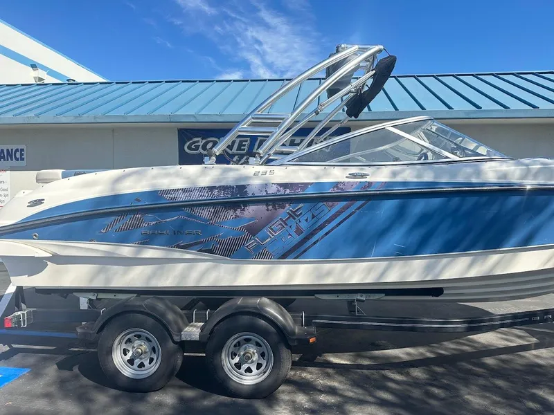 Slide: The Image of 2012 Bayliner 235 Bowrider on trailer, blue and white design, parked outdoors. - 5