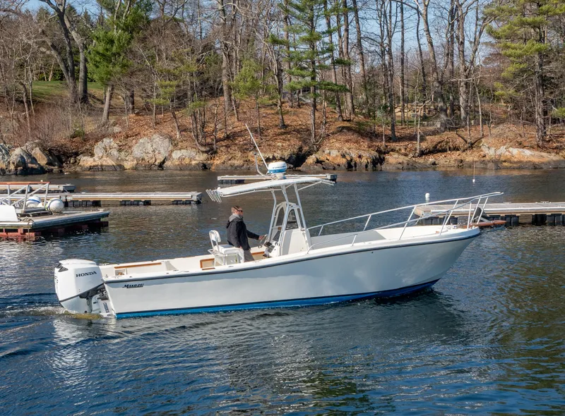 Slide: The Image of 1990 Mako 261 Center Console boat cruising on a calm lake near a wooded shoreline. - 10