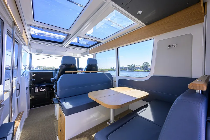 Slide: The Image of 2024 Nimbus C11 boat interior with skylights, blue seating, and wooden table. - 3