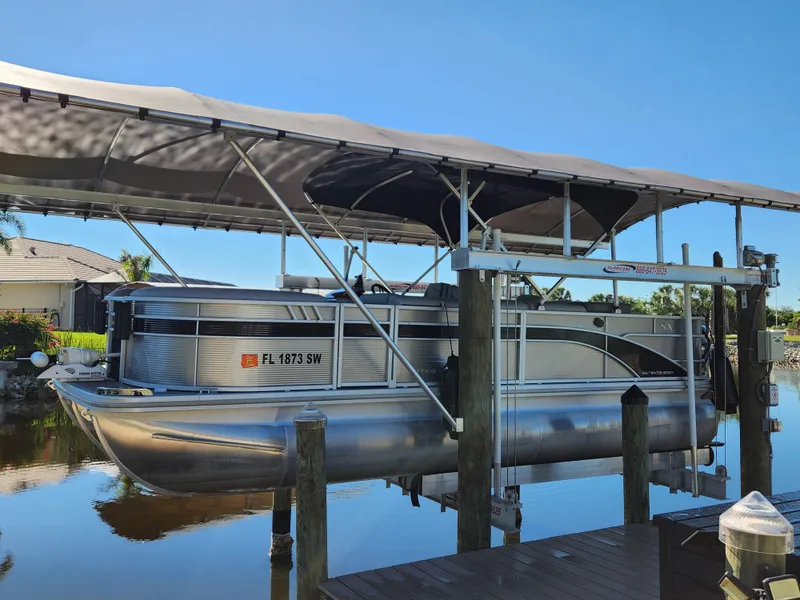 Slide: The Image of 2021 Bennington SX 21 L-Bench pontoon boat docked under canopy. - 2