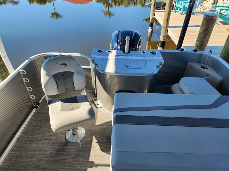 Slide: The Image of 2021 Bennington SX 21 L-Bench pontoon boat interior with seating and helm, docked by calm water. - 8