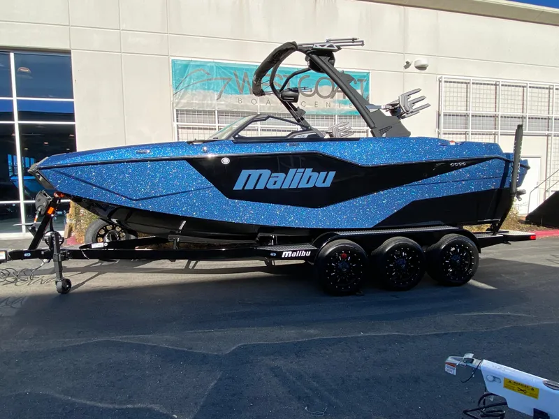 Slide: The Image of 2025 Malibu M230 boat with blue and black design on a trailer. - 1