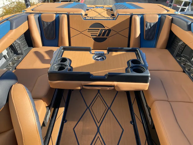 Slide: The Image of 2025 Malibu M230 boat interior with tan seating and built-in cup holders. - 14