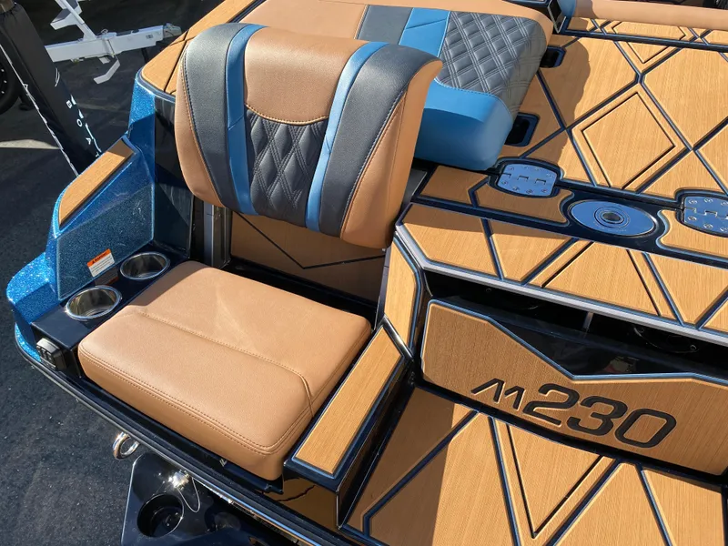 Slide: The Image of 2025 Malibu M230 boat interior with tan and blue seating, cup holders, and stylish design. - 18