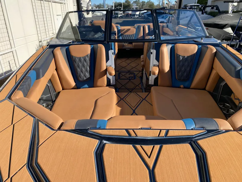 Slide: The Image of 2025 Malibu M230 boat interior with tan and blue seating, modern design, and spacious layout. - 24