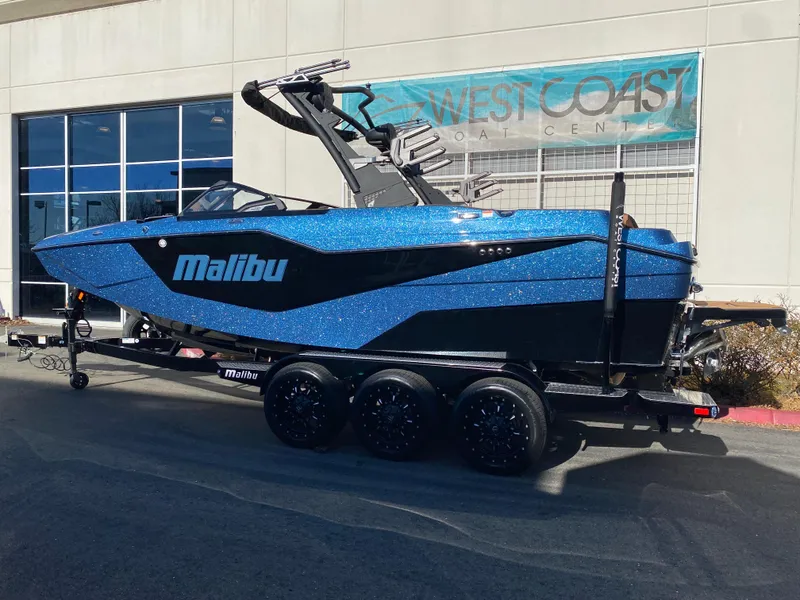 Slide: The Image of 2025 Malibu M230 boat in blue, parked on a trailer outside West Coast dealership. - 4