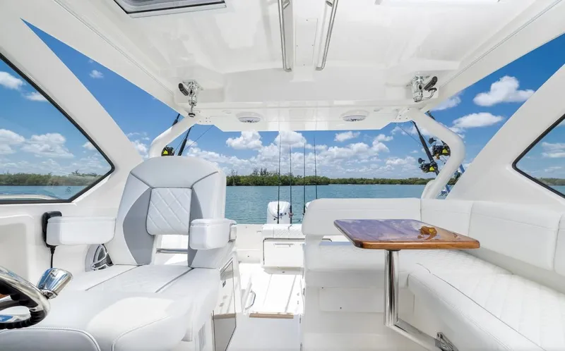 Slide: The Image of 2025 Pursuit OS 325 boat interior with white seating and table, overlooking serene water. - 7