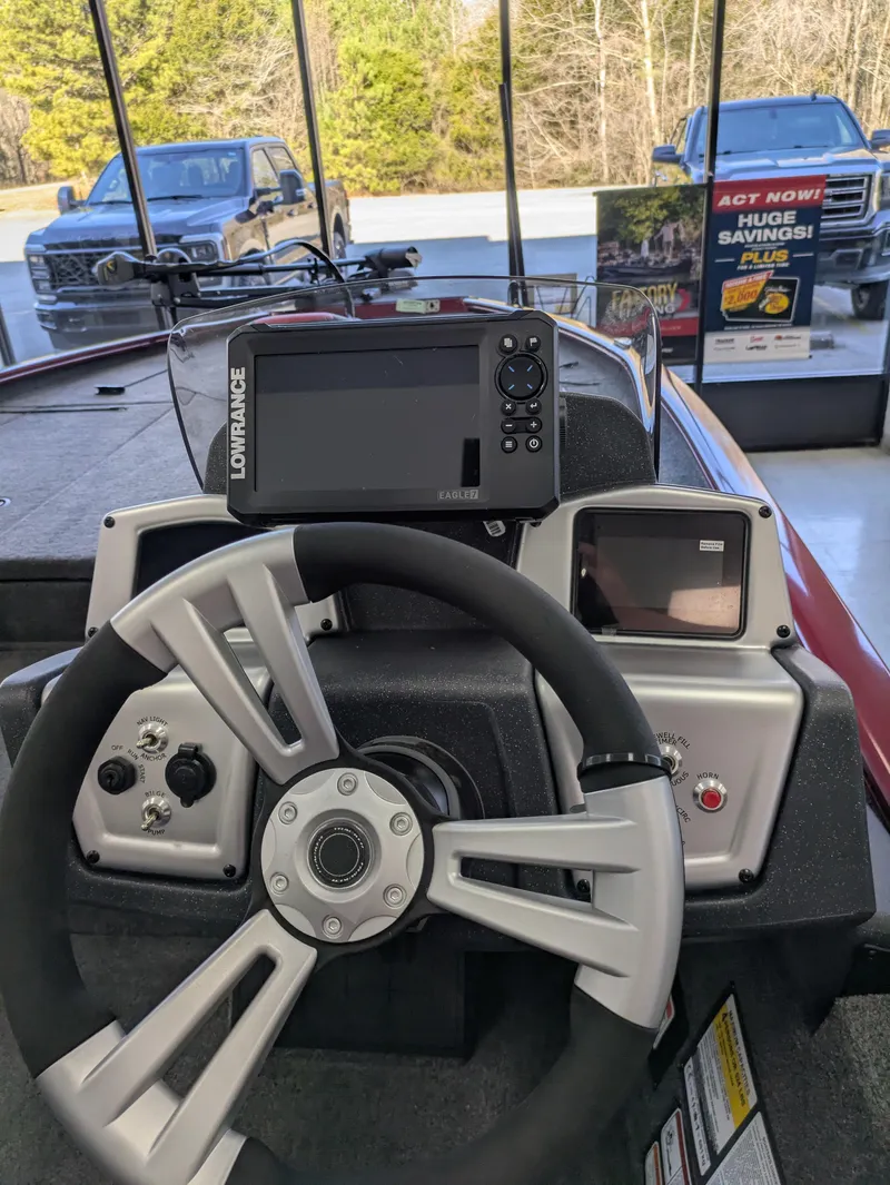 Slide: The Image of Red 2025 Tracker Savage 215 boat with motor, parked on roadside near trees. - 3