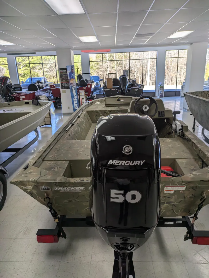 Slide: The Image of 2025 Tracker Grizzly 1648 SC boat with Mercury engine on trailer, parked near trees. - 3