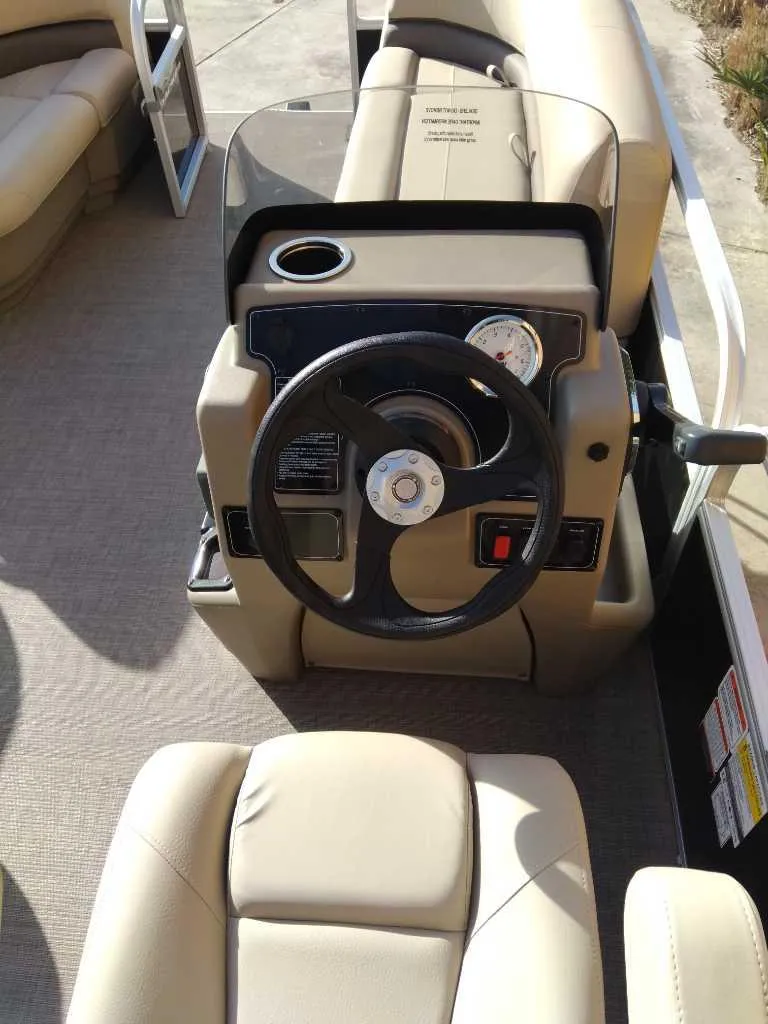 Slide: The Image of 2025 Sun Tracker Party Barge 16 DLX steering console with beige seating and dashboard controls. - 55