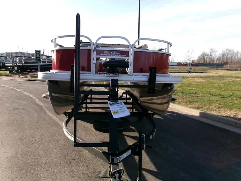 Slide: The Image of 2025 Sun Tracker Bass Buggy 16 XL Select pontoon boat on trailer, parked outdoors. - 2