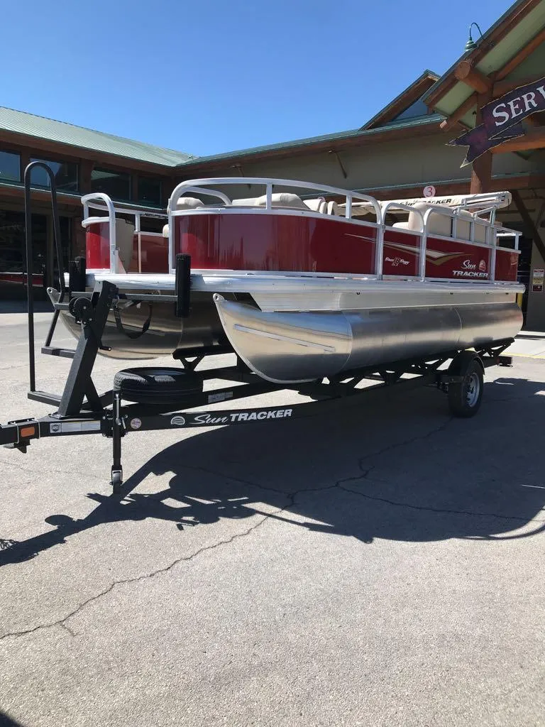 Slide: The Image of 2025 Sun Tracker Bass Buggy 18 DLX pontoon boat on trailer, parked outdoors. - 2