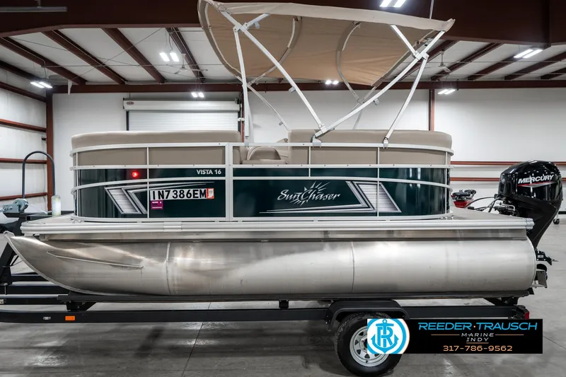 Slide: The Image of 2024 SunChaser 16 Vista pontoon boat in indoor showroom, featuring a canopy and trailer. - 11