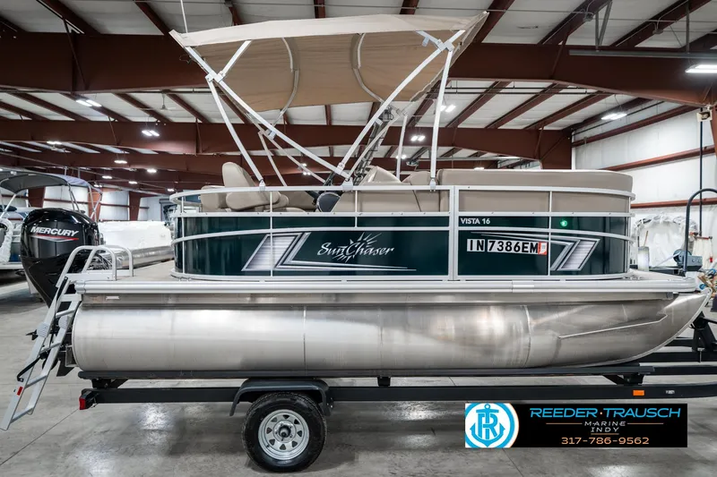 Slide: The Image of 2024 SunChaser 16 Vista pontoon boat in showroom, featuring canopy and trailer. - 7