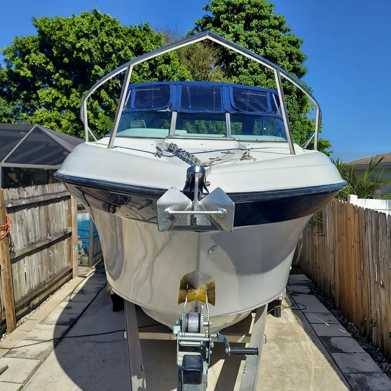 Slide: The Image of 2000 Crownline 242 CR boat on trailer, parked outdoors, surrounded by wooden fence and trees. - 3