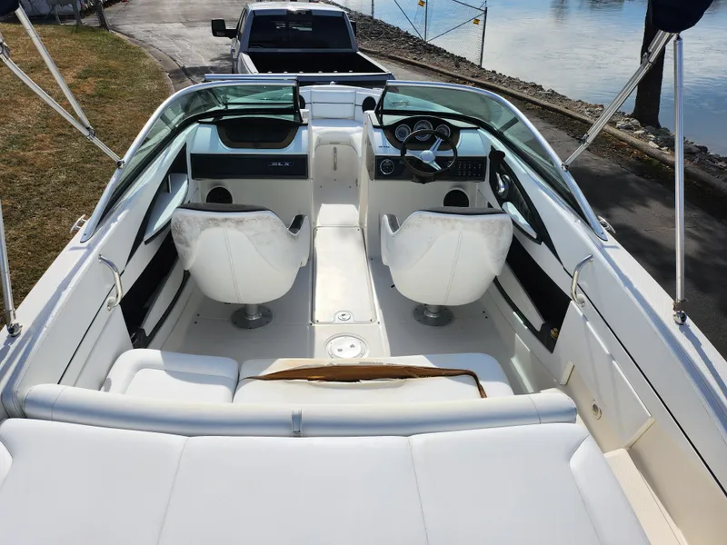 Slide: The Image of 2014 Sea Ray 210 SLX boat interior with white seating and dashboard, docked by the water. - 10