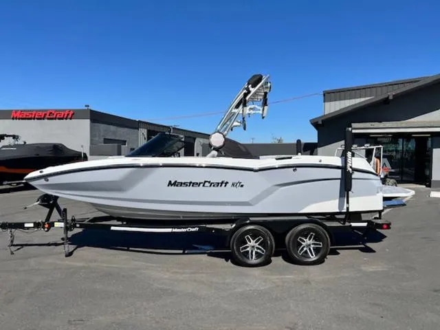 Slide: The Image of 2022 MasterCraft NXT20 boat on trailer, parked outside dealership under clear blue sky. - 1