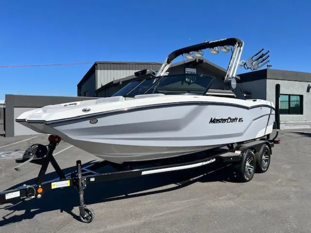 Slide: The Image of 2022 MasterCraft NXT20 boat on trailer, parked outdoors, clear sky background. - 2