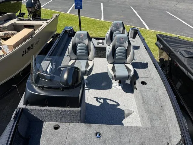 Slide: The Image of 2024 Alumacraft Classic 165 Side Console boat with three seats and a windshield in a parking lot. - 17